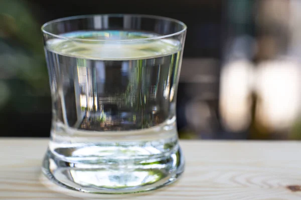 Transparent glass of clean water on wood table in bokeh garden background, Close up & Macro shot, Selective focus, Healthy Drink concept