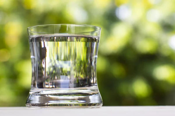 Transparent glass of clean water on wood table in bokeh green garden background, Close up & Macro shot, Selective focus, Healthy Drink concept