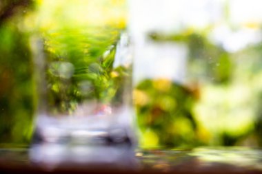 Bokeh yeşil bahçe arka planında yansıma dokusuna yansıyan şeffaf temiz su bardağı, Makro kareyi kapat, Seçici odak, Sağlıklı içecek konsepti