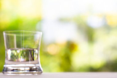 Bokeh yeşil bahçe arka planında ahşap dokusunda saydam temiz su bardağı, Makro kareyi kapat, Seçici odak, Sağlıklı İçecek konsepti