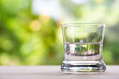 Bokeh yeşil bahçe arka planında ahşap dokusunda saydam temiz su bardağı, Makro kareyi kapat, Seçici odak, Sağlıklı İçecek konsepti