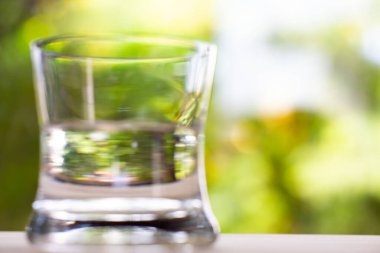 Bokeh yeşil bahçe arka planında ahşap dokusunda saydam temiz su bardağı, Makro kareyi kapat, Seçici odak, Sağlıklı İçecek konsepti