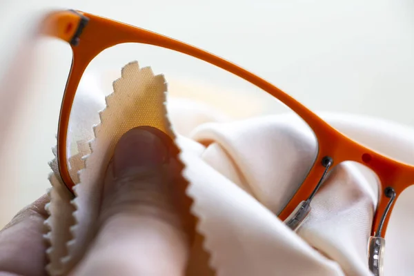Woman's hand cleaning orange eyeglasses by microfibre cleaning cloths, Close up & Macro shot, Selective focus, Optical concept