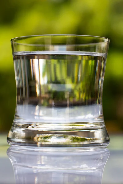 Blurred transparent glass of clean water on white table in bokeh green garden background, Close up & Macro shot, Selective focus, Healthy Drink concept