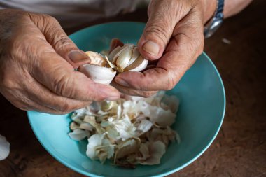 Senior man's hands peeling Garlic or Allium sativum on wood background, Kitchen Process concept clipart