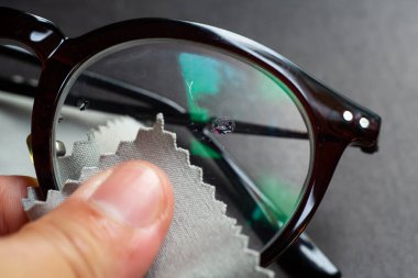 Woman's left hand cleaning shortsighted or nearsighted eyeglasses by microfibre cleaning cloths, On black background, Close up & Macro shot, Selective focus, Optical concept