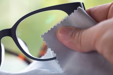 Woman's right hand cleaning grey shortsighted or nearsighted eyeglasses by grey microfibre cleaning cloths, Bokeh green background, Close up & Macro shot, Selective focus, Optical concept clipart