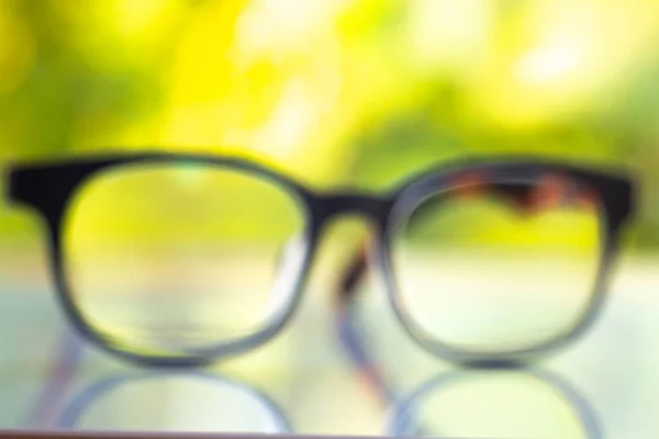 Blurred black shortsighted or nearsighted eyeglasses on white acrylic table, Bokeh green garden background, Close up & Macro shot, Selective focus, Reflection, Optical concept