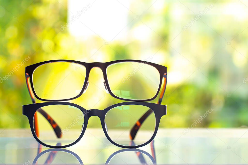 Two black shortsighted or nearsighted eyeglasses on white acrylic table, Bokeh green garden background, Close up & Macro shot, Selective focus, Reflection, Optical concept