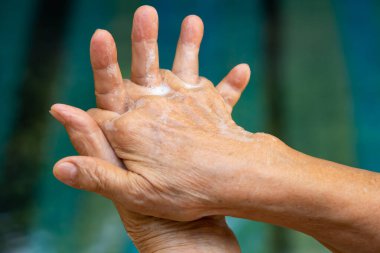 Kıdemli kadının elleri ellerini sabun köpüğüyle yıkıyor. İkinci adımda bokeh mavisi yüzme havuzunda. Yakın çekim, odaklanma, kovid19, Coronavirus, Bakteri, Sağlık Hizmetleri, 7 adım el yıkama.