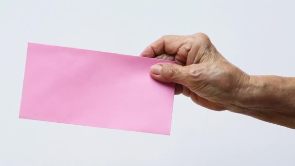 ピンクの封筒を手に持つシニア女性の右手はグレーの背景を持ちます クローズアップとマクロショット ビジネスコンセプト — ストック動画