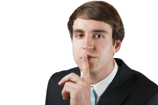 Siyah takım elbiseli, mavi kravatlı, işaret parmağını ağzının önünde tutan ve beyaz arka planda kameraya bakan genç bir adamın kafa ve omuz portresi..