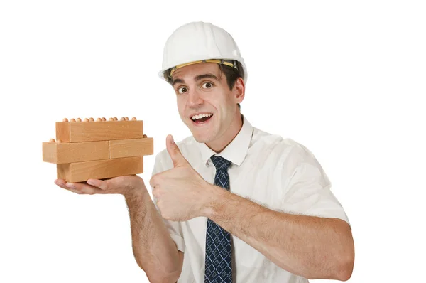 白いシャツ ネクタイ 白い建設現場ヘルメットの若い男の前の胴のビュー右手に積み木の建物のブロックを保持し 白い背景に開いて笑顔で左手の親指を示す — ストック写真