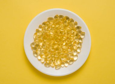 D vitamini kapsülleri sarı zemin üzerinde beyaz bir tabakta.