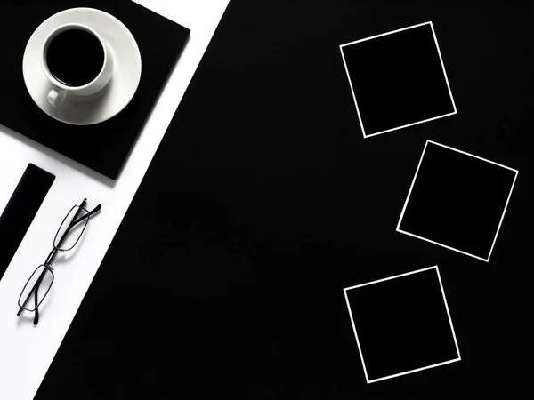 Black and white work space with cup of coffee and empty photo frames. Minimal black work space.