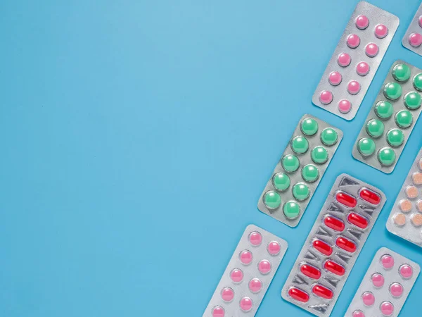 Diferentes píldoras de colores sobre fondo azul, plano — Foto de Stock