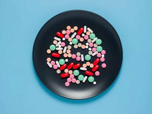 Diferentes píldoras de colores en plato negro, fondo azul . — Foto de Stock