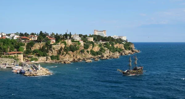 Nave a vela che entra nel porto di Antalya con le scogliere e il centro storico sullo sfondo — Foto Stock