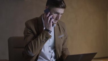 İşadamı bir dizüstü bilgisayar kullanırken telefonda konuşuyor.