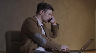 İşadamı bir dizüstü bilgisayar kullanırken telefonda konuşuyor.