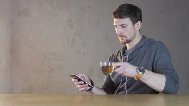 Mladý muž pití čaje a využití jeho mobilní — Stock video