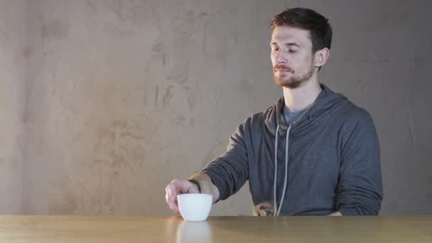 Молодой человек пьет чай из белой чашки — стоковое видео