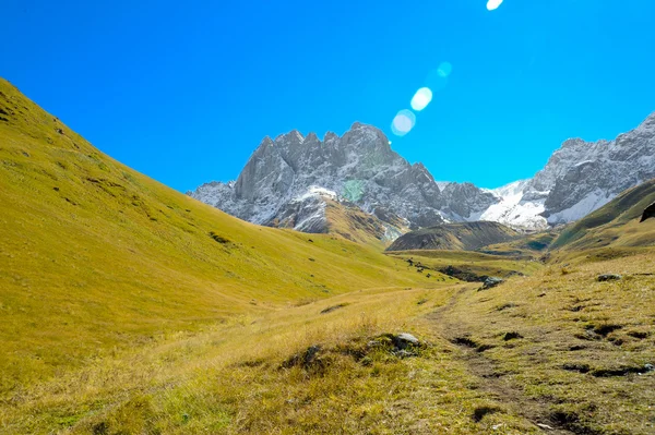 Cáucaso montanhas no verão, grama verde, céu azul e neve no pico Chiukhebi. aldeia Juta, Geórgia — Fotografia de Stock