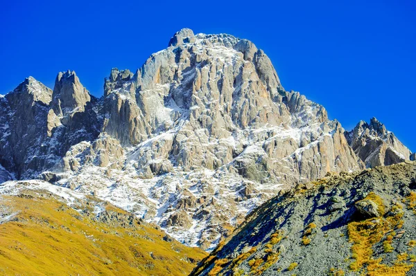 Kaukasus, byn Juta. gröna kulle, blå himmel, berget från stenar och snöiga topp Chaukhebi i sommar. Georgien — Stockfoto
