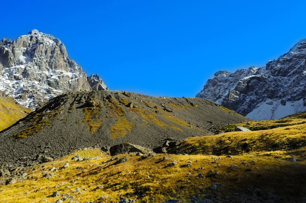 Montañas del Cáucaso, pueblo Juta. colina verde, cielo azul, montaña de piedras y pico nevado Chaukhebi en verano . — Foto de Stock