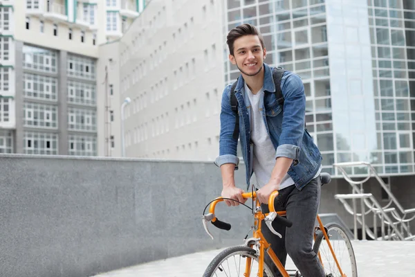 Adam kasabaya mavi kot ceketli bisikletle gidiyor. genç adam turuncu bir düzeltme bisiklet