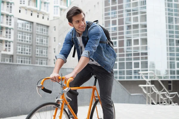 Der Mann fährt mit einem Fahrrad in blauer Jeansjacke in die Stadt. junger Mann ein orangefarbenes Fahrrad — Stockfoto