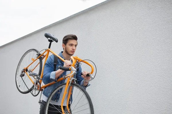 Der Typ in der blauen Jeansjacke trägt ein schulterorangefarbenes Fahrrad. ein junger Mann eine Lösung — Stockfoto