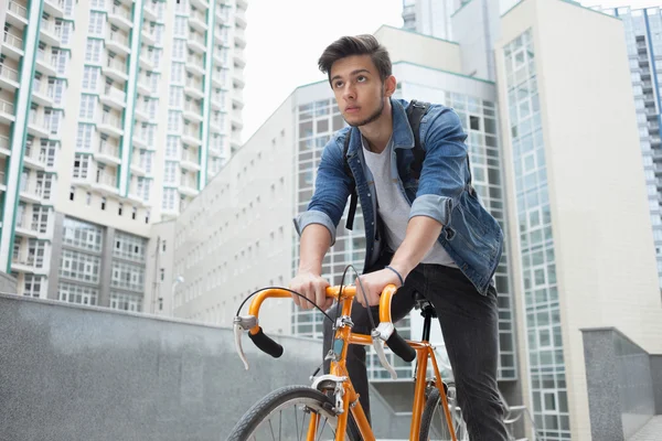 Adam kasabaya mavi kot ceketli bisikletle gidiyor. genç adam turuncu bir düzeltme bisiklet