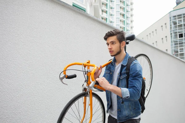 El tipo de la chaqueta vaquera azul lleva en su hombro bicicleta naranja. Un joven un arreglo — Foto de Stock