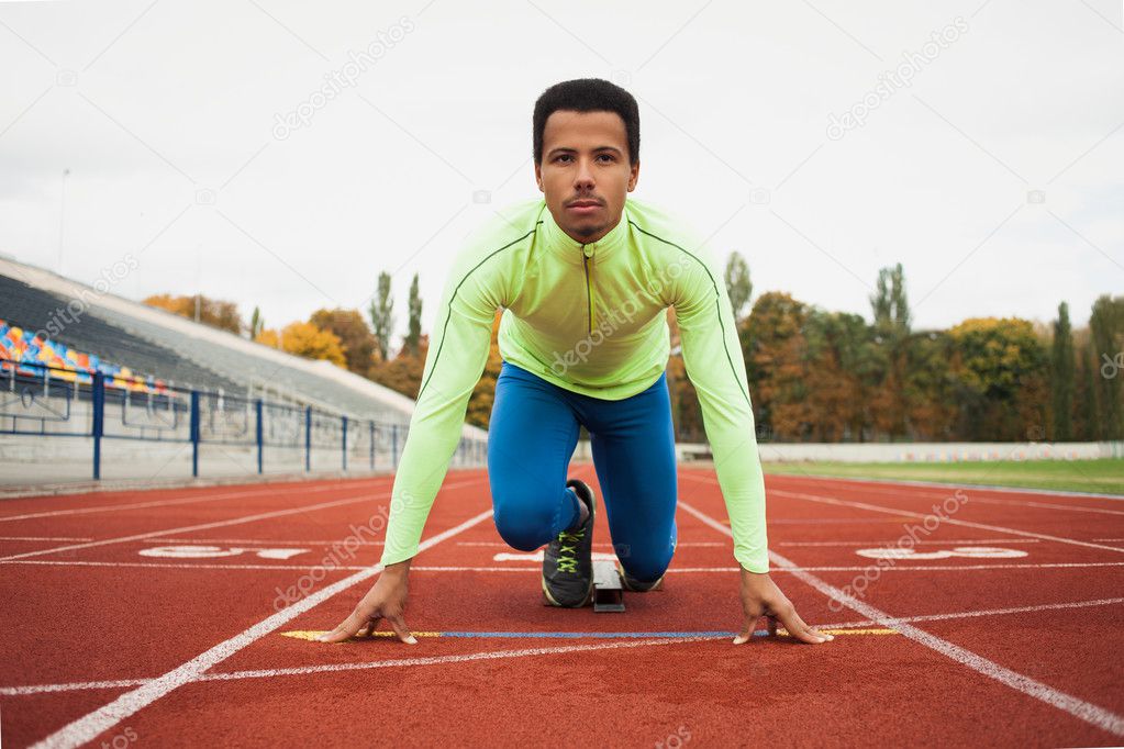 Young sporty man are ready to run on racetrack. Fit well formed people  at large nice modern stadium