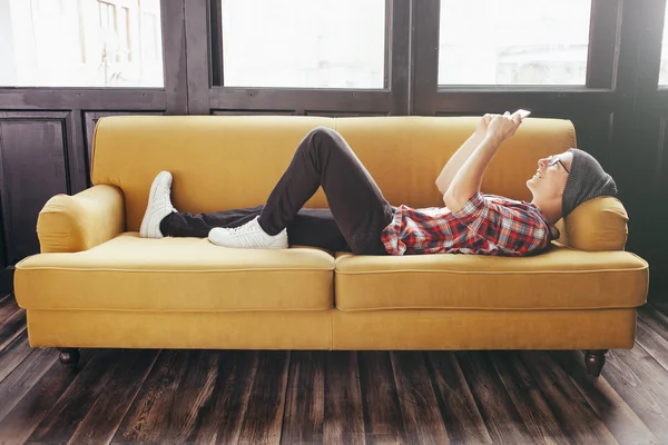 Junger Mann entspannt sich auf Sofa und schaut auf sein Smartphone — Stockfoto