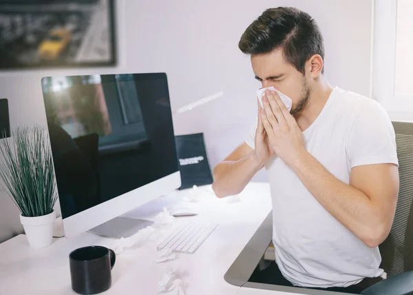 Vista lateral del empleador de pacientes. estornudando en un pañuelo de papel en una oficina cerca de la ventana del ordenador. Diseñador freelancer con frío — Foto de Stock