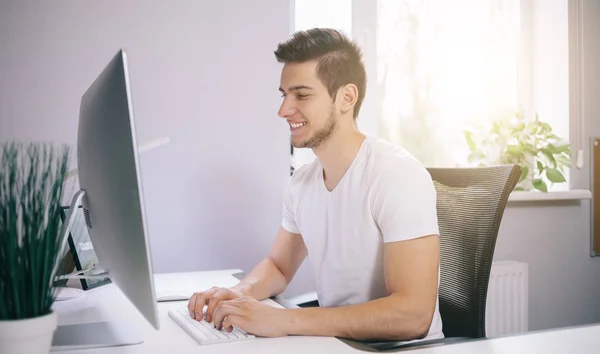 Jongeren zitten in een kantoor op de computer. Freelancer in een wit overhemd. De designer zit voor raam op de werkplek. — Stockfoto