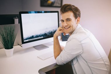 Bir ofiste bilgisayar başında oturan genç bir işçi. Freelancer Beyaz gömlekli. Tasarımcı işyerinde pencerenin önünde oturur.