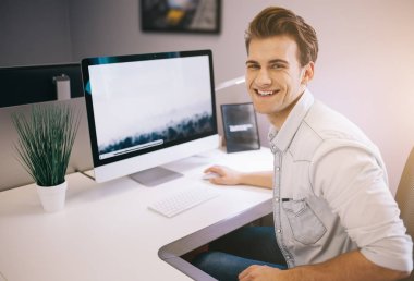 Bir ofiste bilgisayar başında oturan genç bir işçi. Freelancer Beyaz gömlekli. Tasarımcı işyerinde pencerenin önünde oturur.