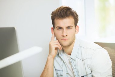 Genç bir programcı kameraya bakıyor. Grafik tasarımcı gelecekteki projeler hakkında düşünüyor. Genç adam ofis bilgisayara windows ile arkasında oturuyor