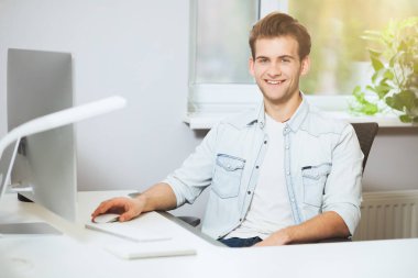 Bir ofiste bilgisayar başında oturan genç bir işçi. Freelancer Beyaz gömlekli. Tasarımcı işyerinde pencerenin önünde oturur.