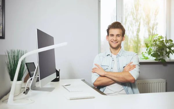 Молодий працівник сидить в офісі за комп'ютером. Фрілансер у білій сорочці. Дизайнер сидить перед вікном на робочому місці . — стокове фото
