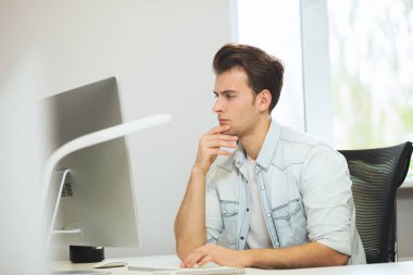 Genç bir programcı kameraya bakıyor. Grafik tasarımcı gelecekteki projeler hakkında düşünüyor. Genç adam ofis bilgisayara windows ile arkasında oturuyor