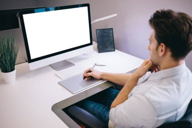 Bir ofiste bilgisayar başında oturan genç bir işçi. Freelancer mavi gömlekli. Tasarımcı işyerinde pencerenin önünde oturur.
