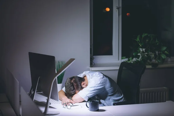 Slapende jonge man aan het werk op de computer's nachts in donkere kantoor — Stockfoto