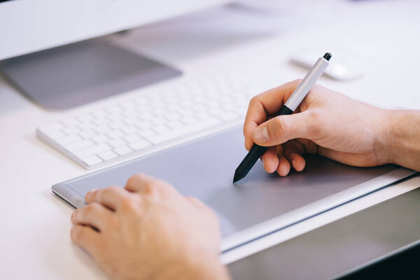 Young worker sitting in an office at the computer. Freelancer in a blue shirt. The designer sits in front of window in the workplace.