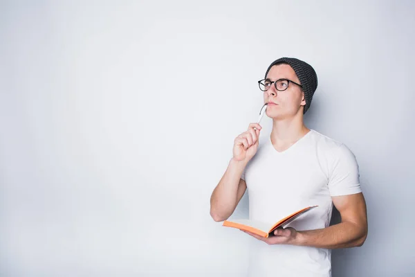 Nachdenklicher männlicher Student hält Notizbuch in der Hand und blickt isoliert auf weißem Hintergrund hoch. — Stockfoto