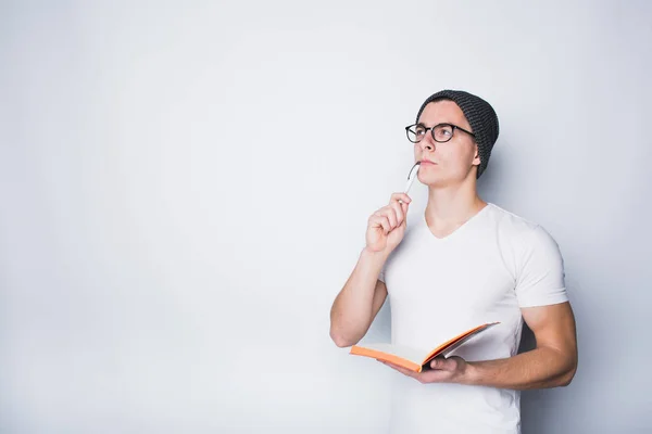 Düşünceli erkek öğrenci holding defter ve bakmak beyaz bir arka plan üzerinde izole.