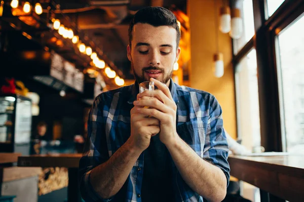 Junger Mann sitzt im Restaurant und probiert ein warmes Getränk. — Stockfoto